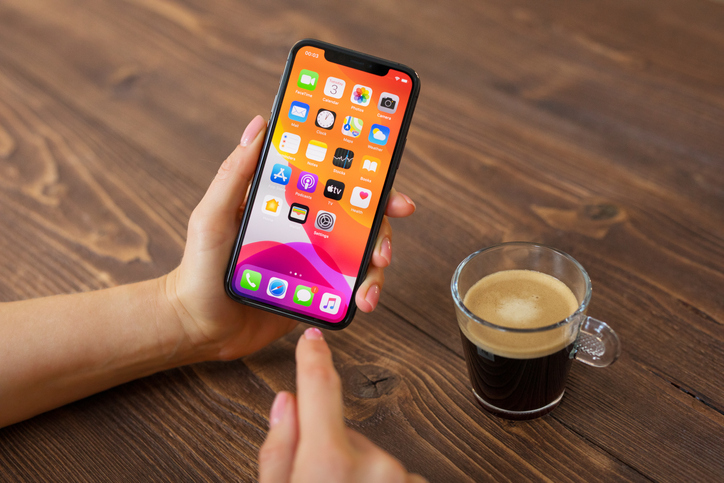 A person using an iPhone at a table drinking a coffee